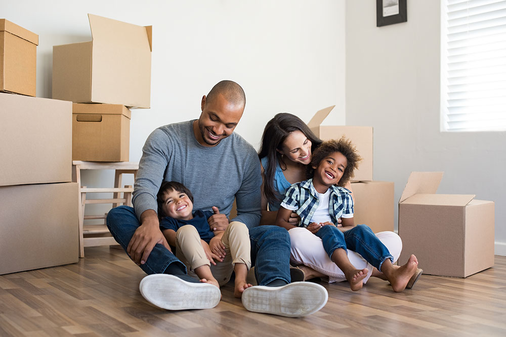 family of four sitting in new home with boxes around them