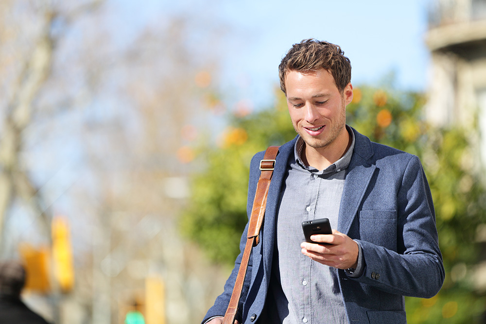 young businessman walking while looking at mobile phone