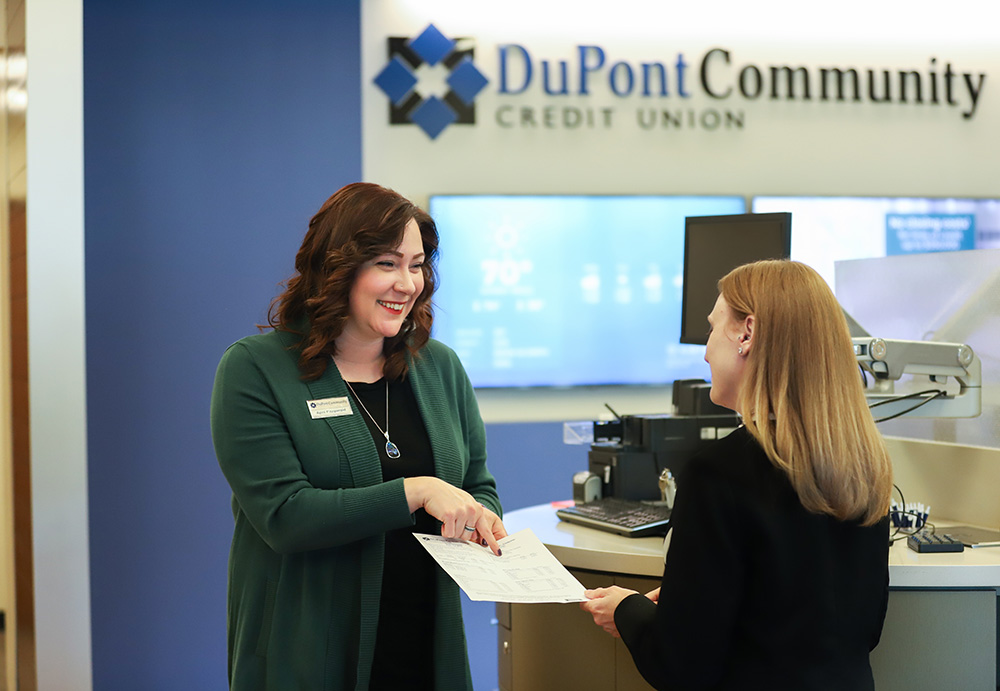A female DCCU employee is smiling as she assists a member with a transaction