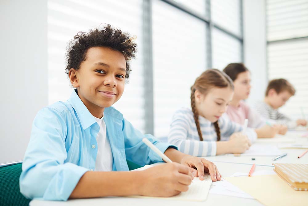 young male student in classroom smiling while doing school work