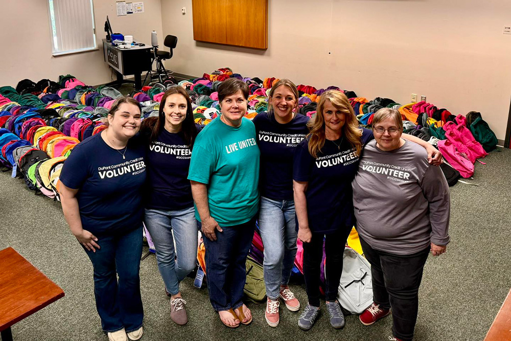 A group of volunteer from DCCU pose in front of a group of backpacks during the Harrisonburg-Rockingham United Way's annual Tools for School school supply drive. 