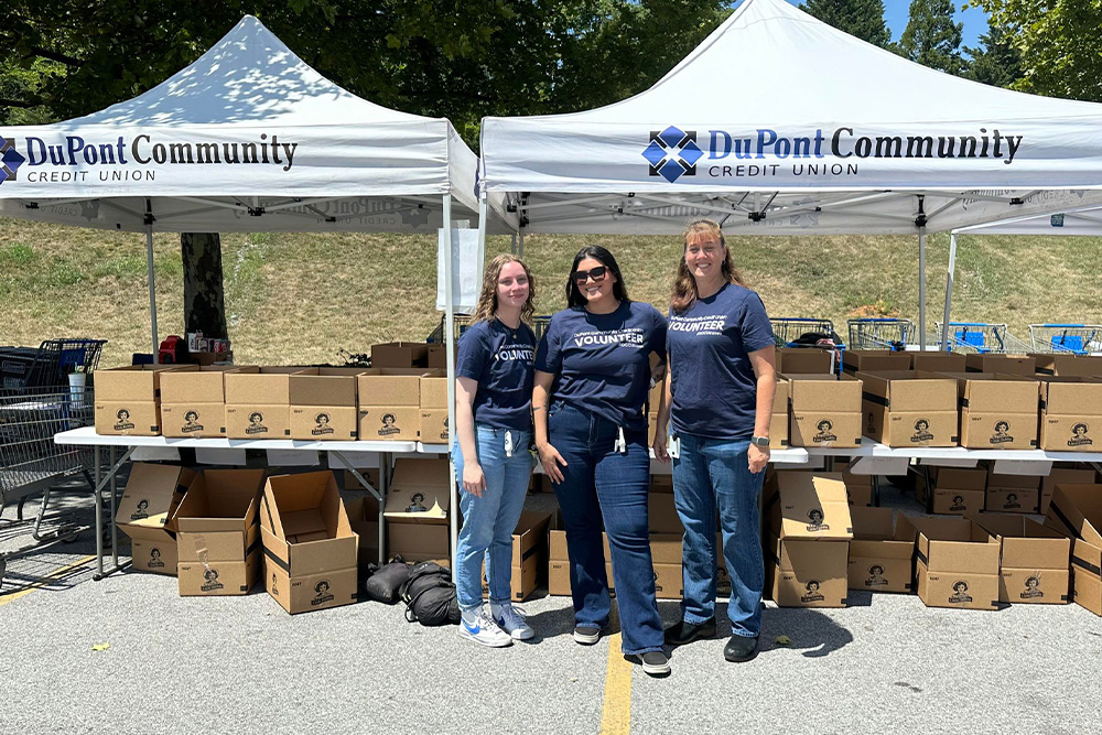 A group of DCCU employees pose in front of boxes during the United Way's annual Stuff the Bus school supply drive. 