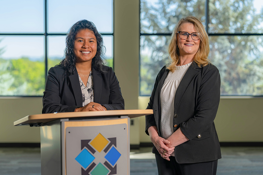 DCCU Cares Foundation team members, Jennifer Arteaga-Vargas and Sarah Landram smile for the camera behind a podium