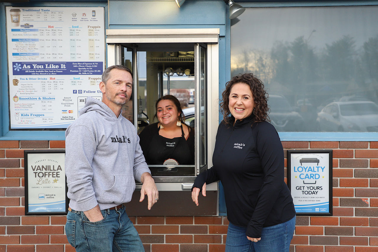 Bobby and Megan Collier, owners of micah's coffee stand in front of their coffee shop with a barista. 
