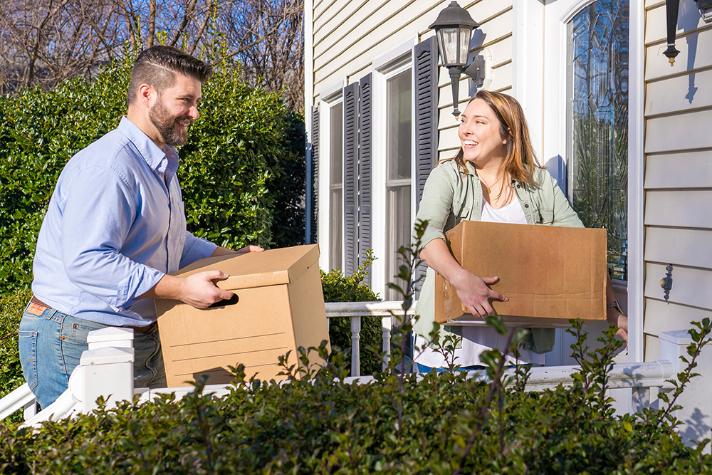 Couple moving boxes into house