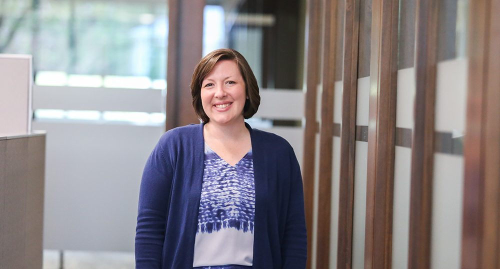 DCCU employee woman stands beside wall, smiling.