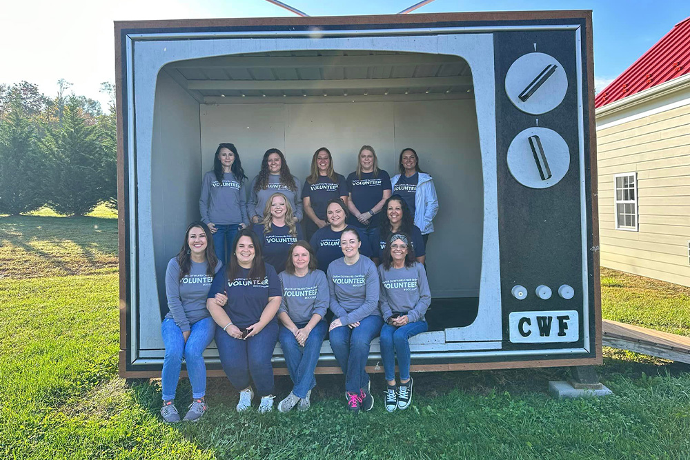 DCCU employees stand inside a large vacant television set and smile for the camera as they volunteer with CampLIGHT in Waynesboro.
