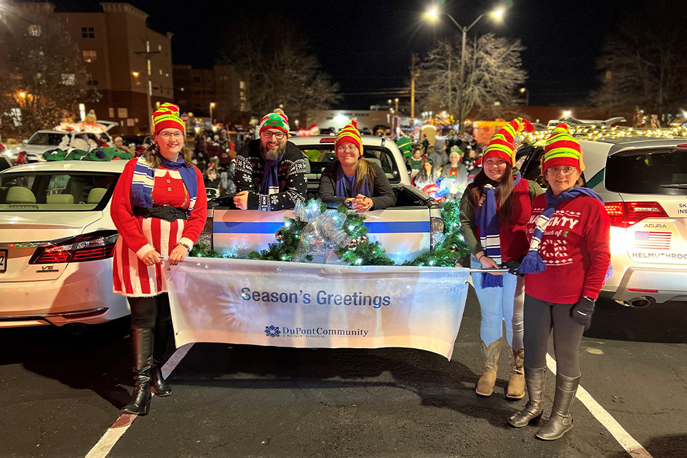 DCCU employees stand behind a 'Season's Greetings' sign at the 2022 Harrisonburg City holiday parade. 