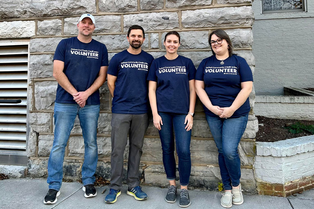 Four DCCU employees stand against a rock wall