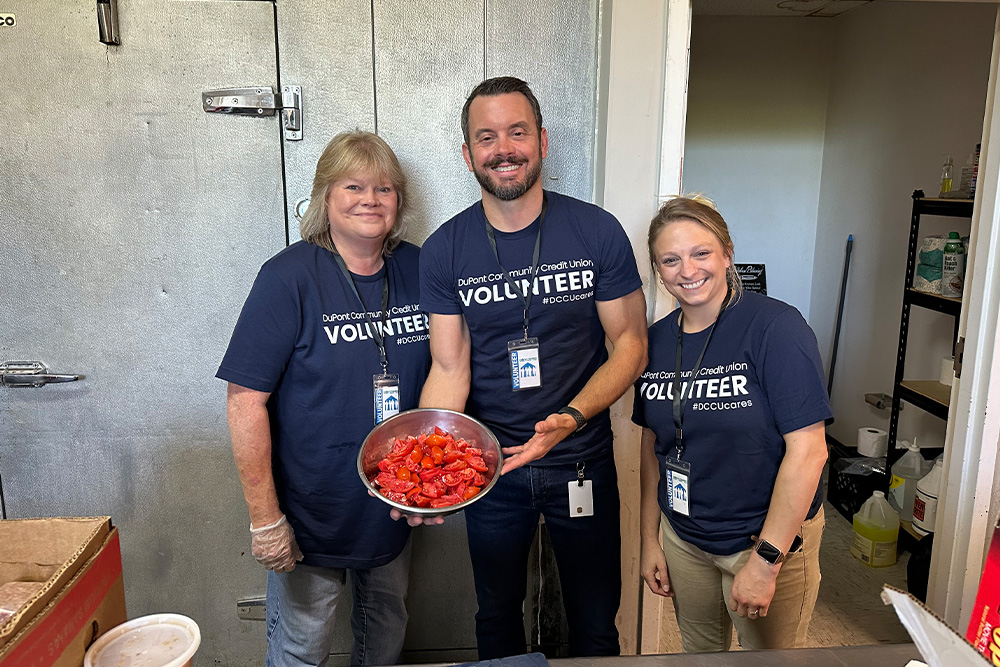 Three DCCU employees pose and smile for the camera as they volunteer at the Valley Mission