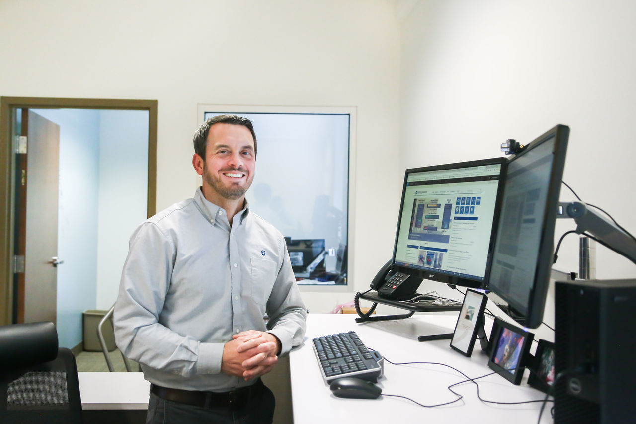 A young professional man casually leans against at desk.