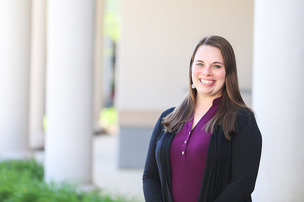 Female DCCU employee smiling outside in front of pillar