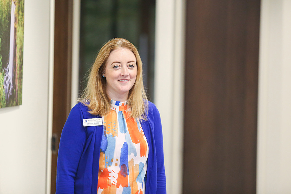 DCCU Corporate Administrator, Jennifer, stands in a hallway, smiling for the camera