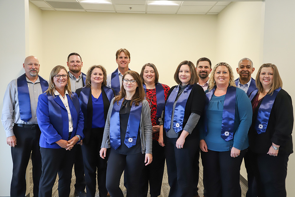 A group of DCCU employees stand together following a graduation ceremony from the Leadership Impact Journey program. 