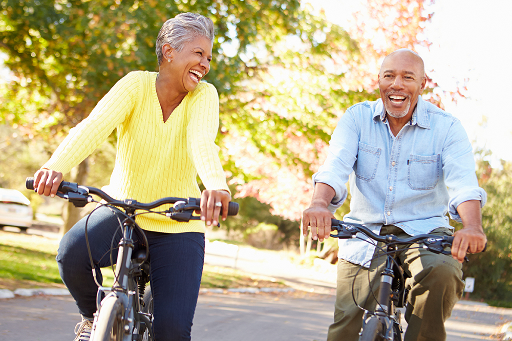 An elderly man and woman ride bicycles together. They are smiling