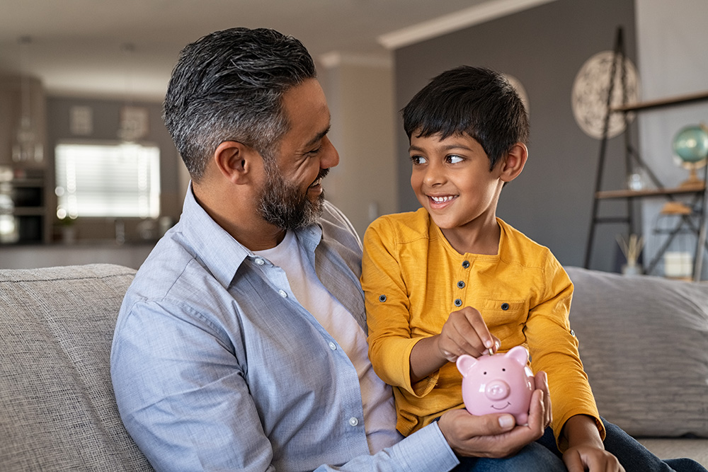 dad and son putting money in a piggy bank together