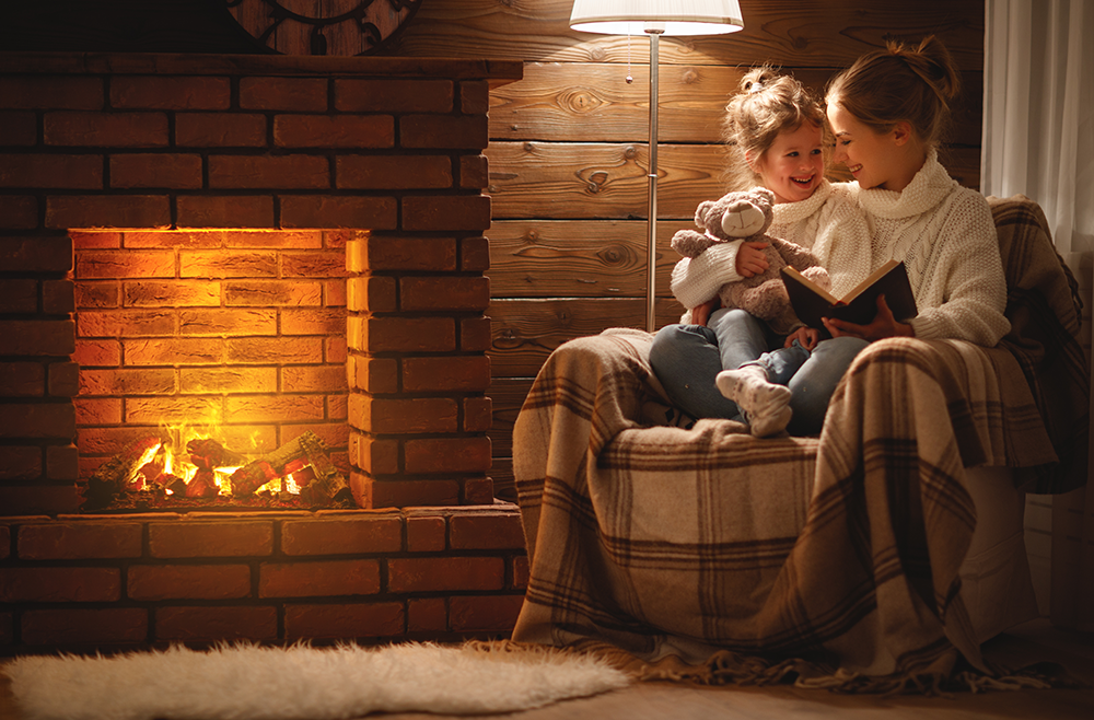 mom and daughter reading book together by the fireplace