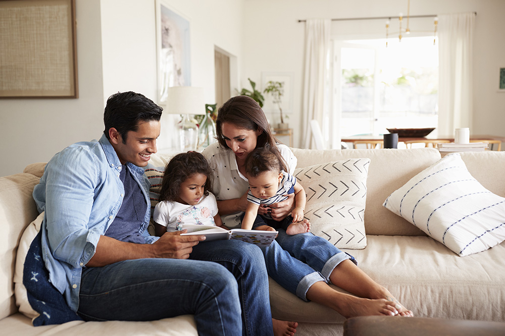 Family of four looking at a book together on couch