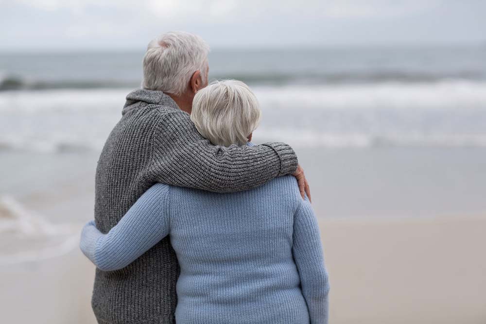elderly couple looking at ocean on the beach