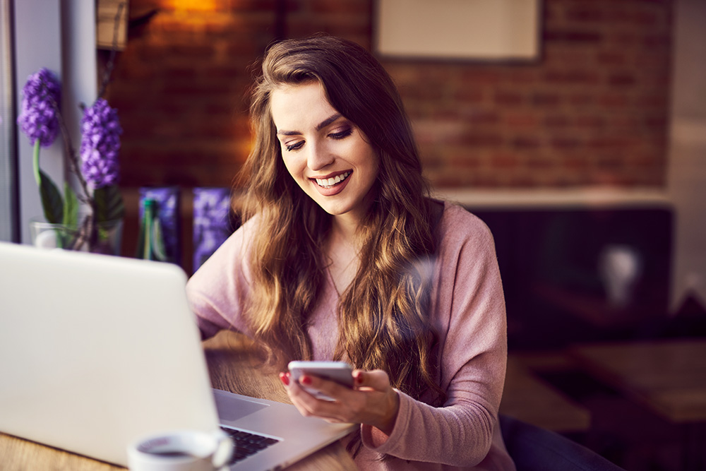 young woman looking at phone and laptop