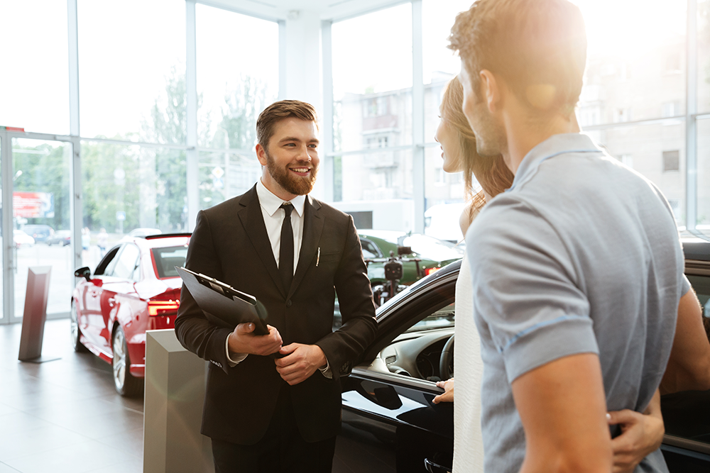 car salesman talking with couple in a dealership