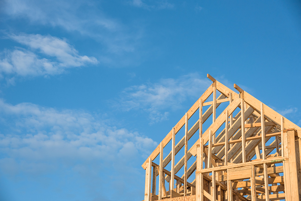 Wooden framework of home stands against a cloudy, blue sky