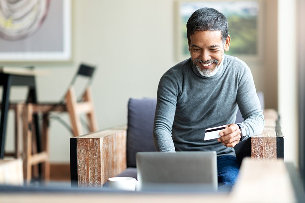 Smiling man holds credit card while sitting in front of laptop computer