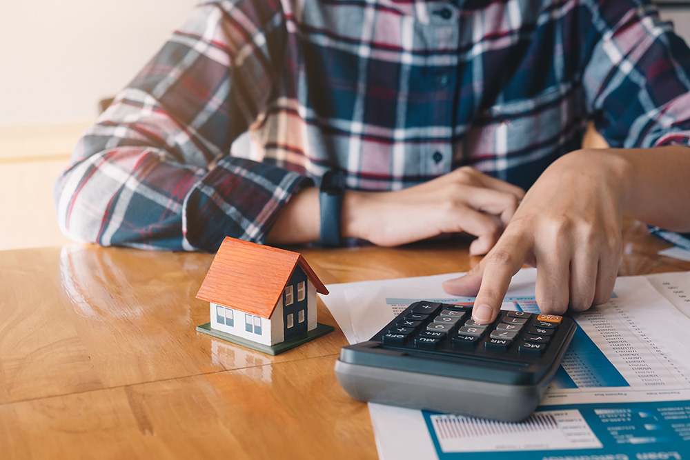 Man using calculator with small house toy on desk
