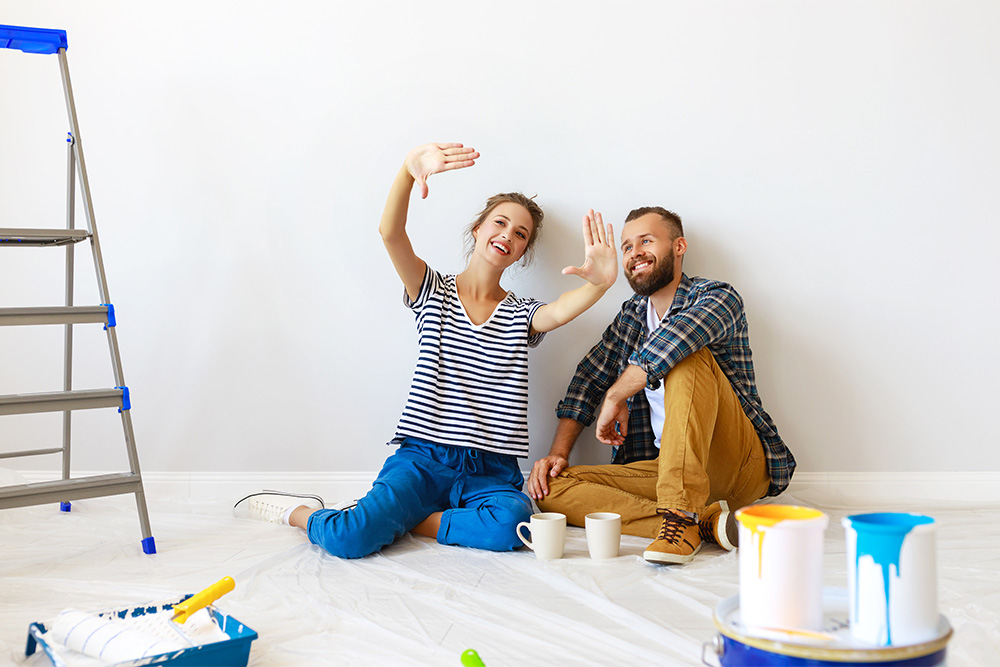 Young woman and young man lean against wall in unfinished room, smiling and sitting