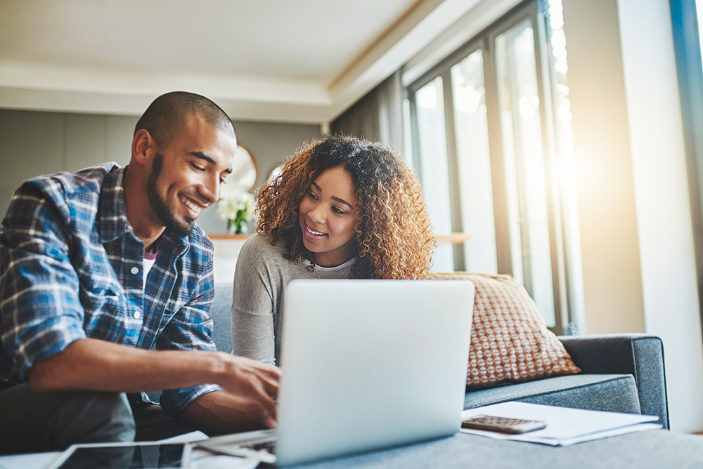 A man and a woman sit behind a laptop computer. They are both smiling. 