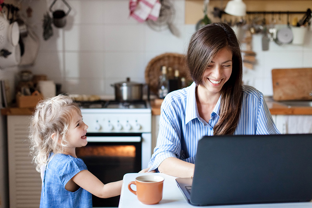 mom on computer while laughing with young daughter