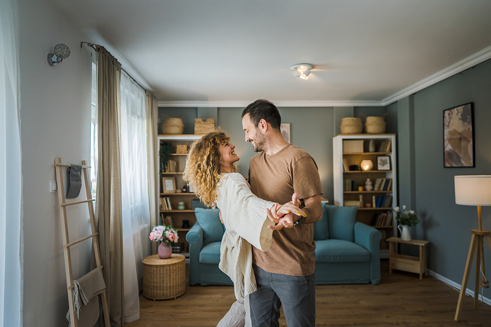 A young man and a woman dance together in their living room.