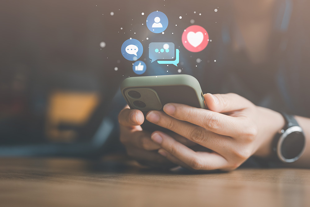 A person holds a smartphone with social media reactions superimposed over the image. 