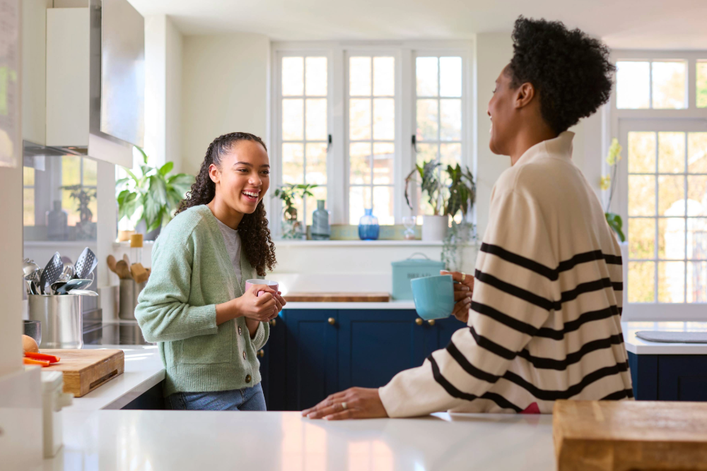 A young woman and her mother smile at each other in a kitchen. 