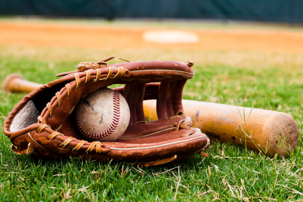 A picture of a baseball mitt, ball, and bat laying on a baseball field. 