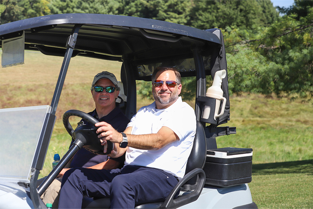 DCCU President/CEO, Steve Elkins, and Chief Operating Officer, Barry Smith, smile for the camera from a golf cart at the DCCU Cares Foundation golf tournament in September 2025.