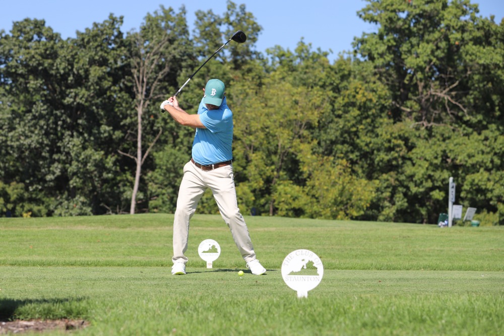 A man in a blue shirt hits a golf ball. 