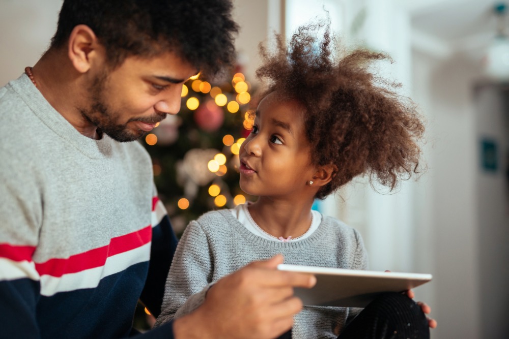A man and small child look at each other as the child holds a tablet.
