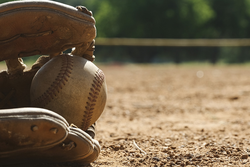 A close-up picture of a weathered baseball sitting inside a baseball mitt, laying on a baseball field.