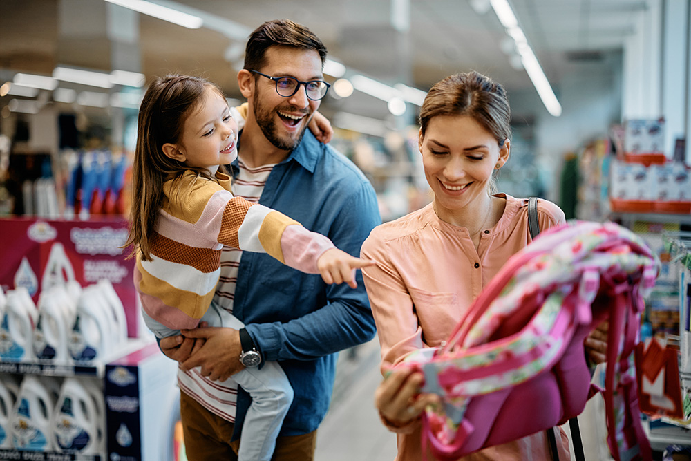 Mom and dad looking at backpacks in store with daughter