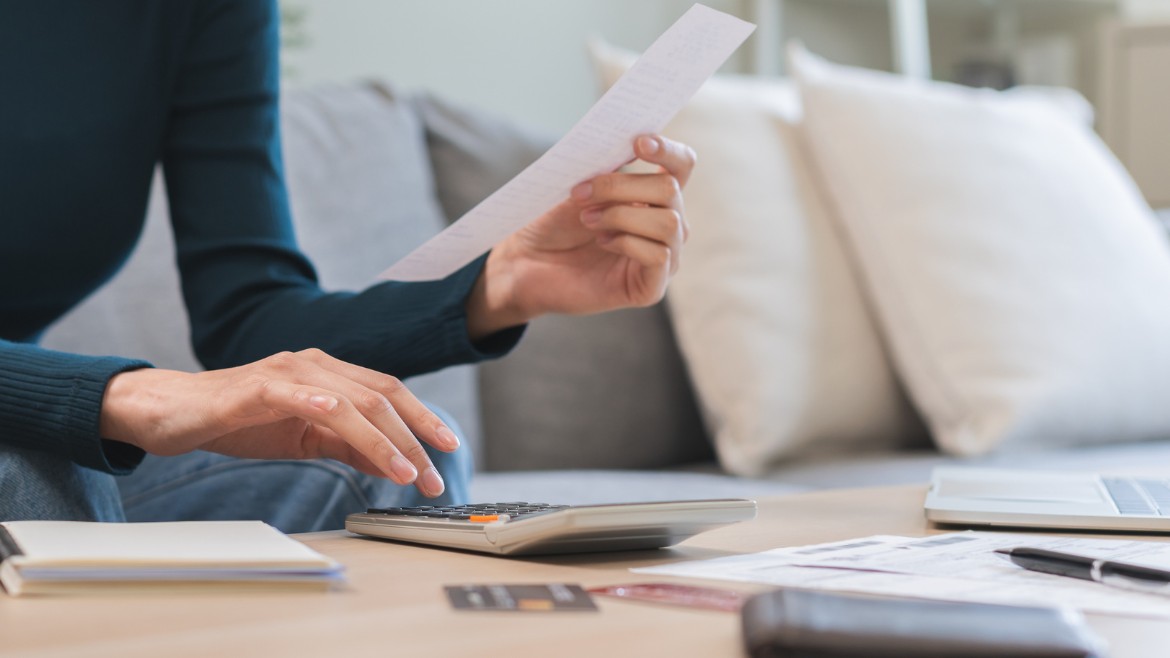 A person sits at a table, calculating the total of a receipt in their hand. 