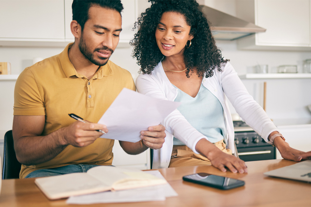 A man and woman sit a kitchen table, discussing finances