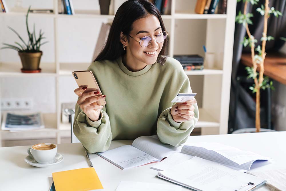 young woman looking at credit card while holding her mobile phone