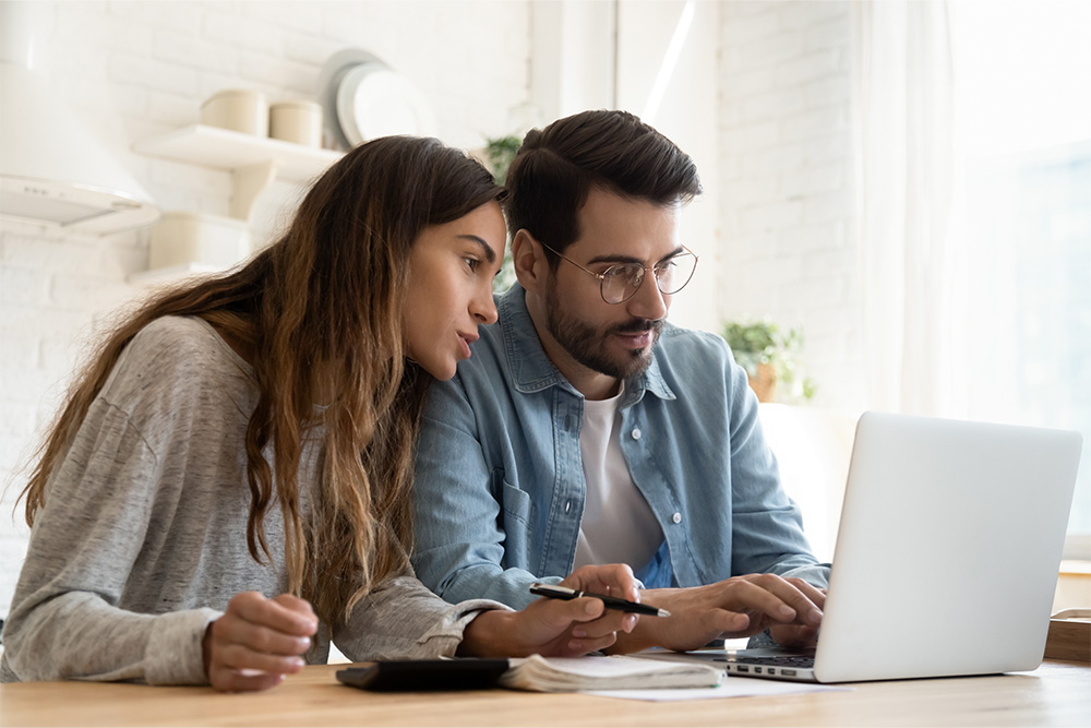 A woman and man sit behind a laptop with a calculator and pen, working on their finances. 