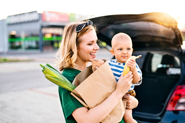 Mother holding infant in parking lot with groceries