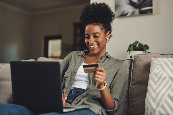 Smiling woman sitting on couch shopping on laptop while holding credit card