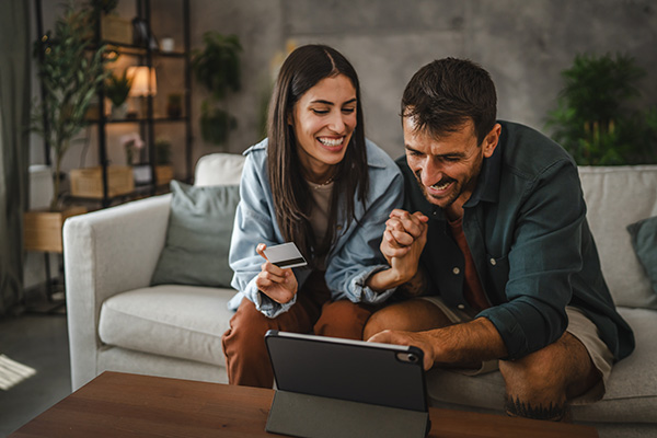 happy couple looking at tablet while holding credit card