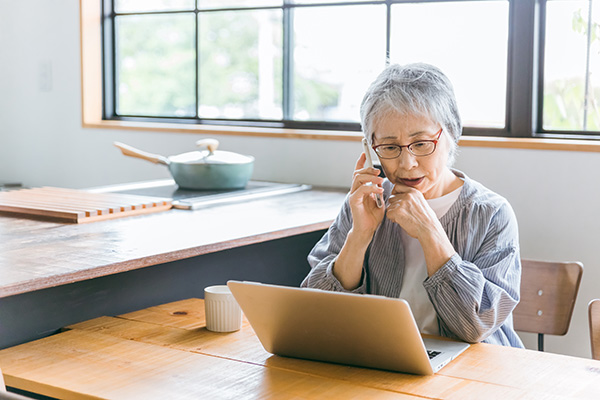 older woman on the phone while looking nervously at laptop