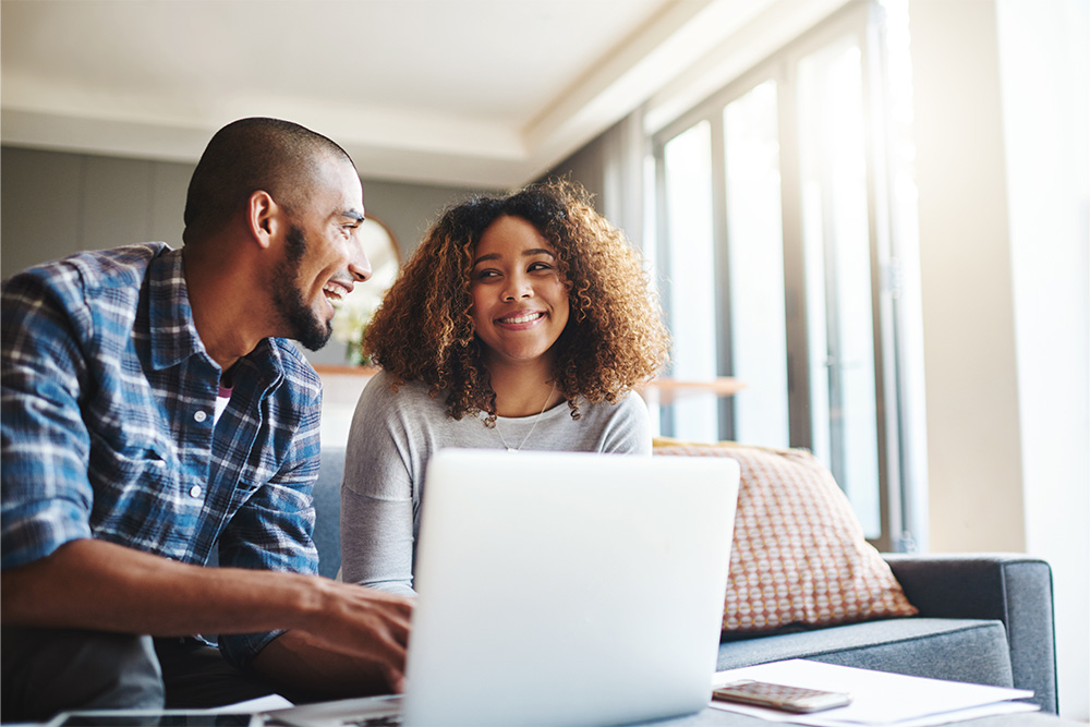 A man and woman smile at each other as they sit behind a laptop. 