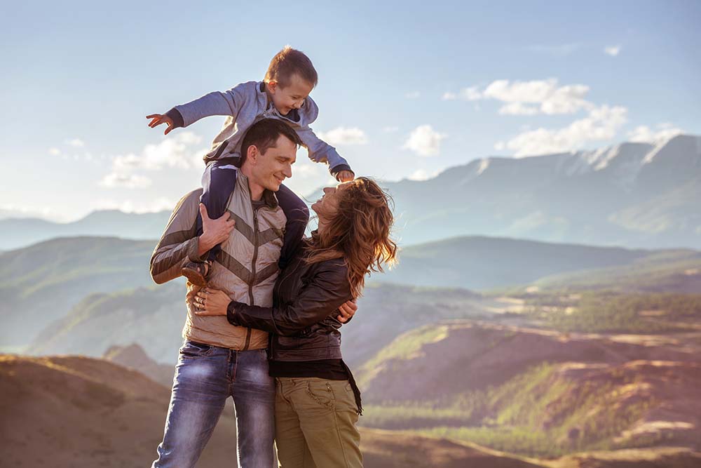 family of three standing in front of scenic mountain views